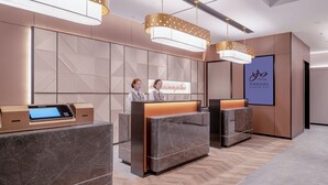 A hotel reception area with a modern design, featuring a reception desk with a digital screen, two receptionists, and a large sign displaying the hotel name. - Zhangjiajie Homeinn Plus Hotel (Zhangjiajie)