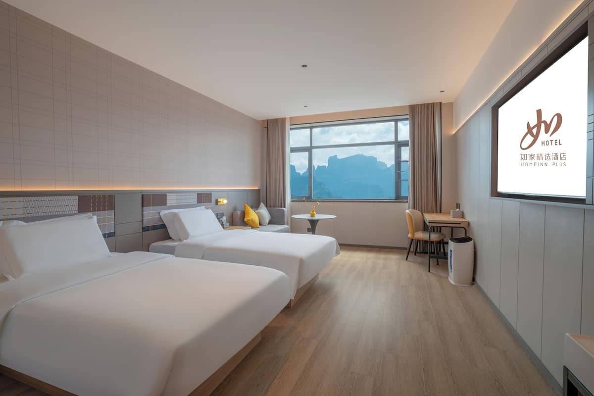 Ein Hotelzimmer mit zwei Betten, einem kleinen Tisch, einem Stuhl und Bergblick durch ein großes Fenster.