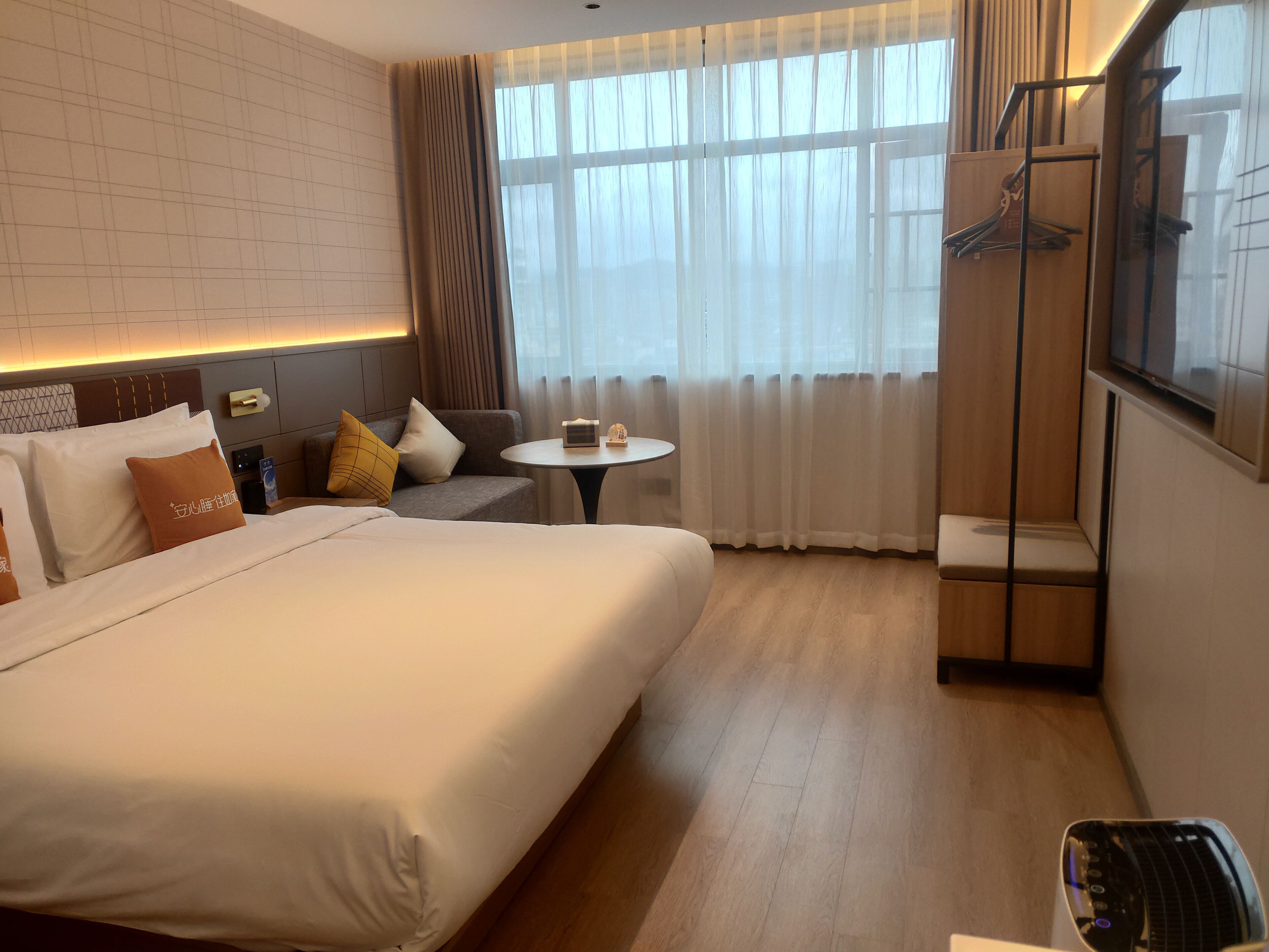A hotel room with a large bed, a small round table, a sofa, a TV, and a wardrobe.
