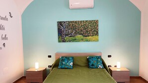 Ein Schlafzimmer mit grüner Bettdecke, zwei passende Kissen, einer Wand-Klimaanlage und einem Bild von Baum und Landschaft.