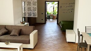 Ein Wohnzimmer mit einer Couch, einem Couchtisch, einem Esstisch mit Stühlen, einem weißen Schrank und einer Wand mit einer dekorativen Schrift.