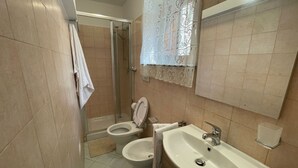 Ein Badezimmer mit zwei Toiletten, einer Dusche, einem Waschbecken und einem Spiegel.