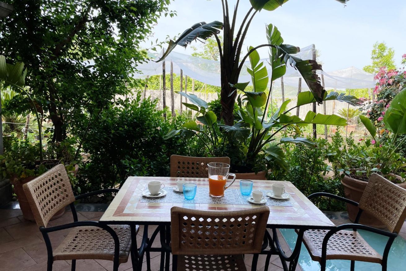 Une table dressée à l’extérieur, avec des chaises, une nappe et un verre de jus d’orange.