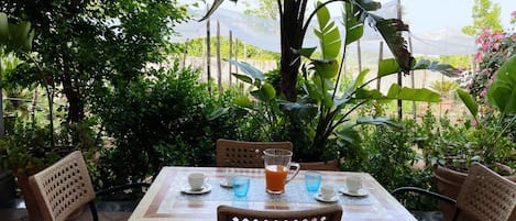 A table set outdoors with chairs, a tablecloth, and a glass of orange juice.