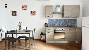 Eine kompakte Küche mit Essbereich, mit Marmor-Spritzschutz, Edelstahlgeräten und hellem Holzkorpus.
