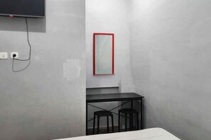 A room with a flat-screen TV mounted on the wall, a small table with two stools, and a red-framed mirror. - Puspita Homestay Mitra RedDoorz (Pondok Melati)