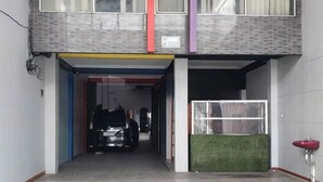 A building entrance with a covered walkway, a car parked inside, and a green artificial turf area. - Puspita Homestay Mitra RedDoorz (Pondok Melati)