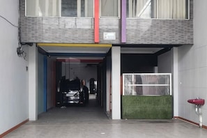 A building entrance with a covered walkway, a car parked inside, and a green artificial turf area. - Puspita Homestay Mitra RedDoorz (Pondok Melati)