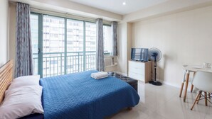A hotel room with a large bed, a desk, a chair, a television, and a window with curtains. - Comfy condo. Best location on Shaw Blvd, front of Shang Mall. Short walk to SM. (Mandaluyong City)