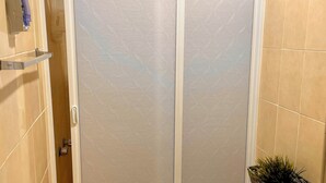 Un baño con puerta de vidrio satinado, un perchero y una planta en maceta.