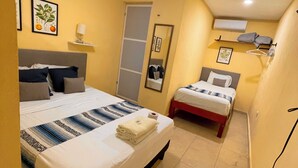 Habitación de hotel con dos camas, un espejo, una estantería con lámpara y un aire acondicionado.