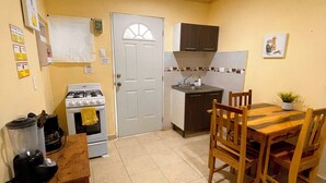 Una cocina compacta con estufa, horno y lavamanos, una mesa de madera con sillas, y una pequeña planta en maceta sobre la mesa.