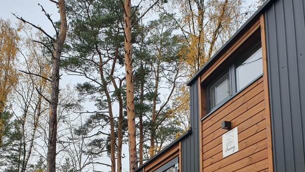 Une cabane avec une terrasse, deux chaises, un barbecue et un panneau indiquant « 100 % isolé(e) ».