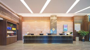 A modern reception desk with a wooden finish, a large vertical light fixture, and a world map mural on the wall. - Zhangjiajie Hero Boutique Hotel (Zhangjiajie)