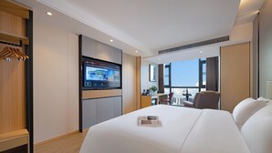 A hotel room with a large bed, a desk with a chair, a television mounted on the wall, and a view of the city through large windows. - Zhangjiajie Hero Boutique Hotel (Zhangjiajie)