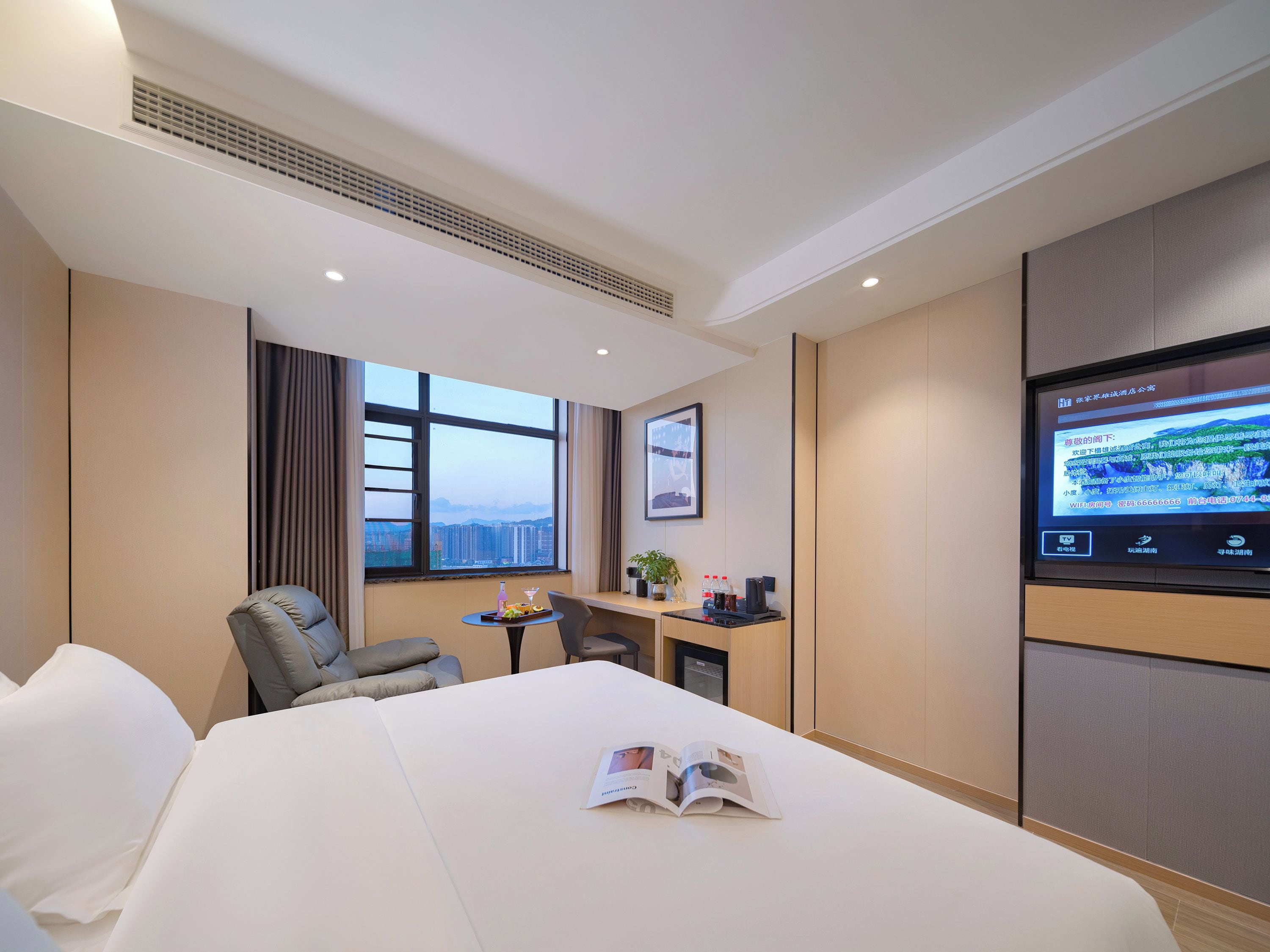 A hotel room with a bed, a desk, a chair, a TV, and a window with a city view.