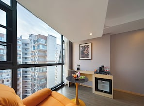 A modern apartment with a large window, a small round table with a tray of fruit, a sofa, and a kitchenette. - Zhangjiajie Hero Boutique Hotel (Zhangjiajie)