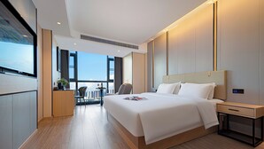 A modern hotel room with a large bed, a desk, a chair, and a view of the cityscape through large windows. - Zhangjiajie Hero Boutique Hotel (Zhangjiajie)
