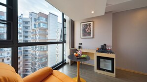 A modern apartment with a large window, a small round table with a tray of fruit, a sofa, and a kitchenette. - Zhangjiajie Hero Boutique Hotel (Zhangjiajie)