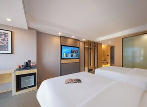 Ein modernes Hotelzimmer mit einem großen Bett, einem flachbildfernseher an der Wand, einem Schreibtisch mit Kaffeemaschine und einem kleinen Kühlschrank.