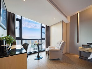 A modern hotel room with a large window, a dining table, a sofa, and a small desk. - Zhangjiajie Hero Boutique Hotel (Zhangjiajie)