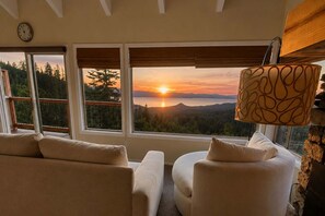A room with a sofa and armchair facing a large window with a view of a sunset over a mountainous landscape. - Breathtaking Lake Views | Nearby Stagecoach Lift (Stateline)