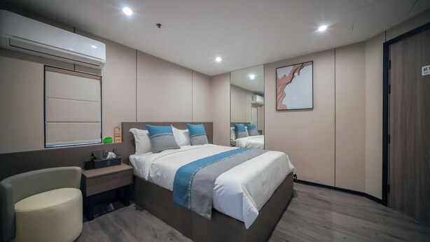 Una habitación de hotel moderna con una cama grande, mesitas de noche, una silla, un espejo y un aire acondicionado.