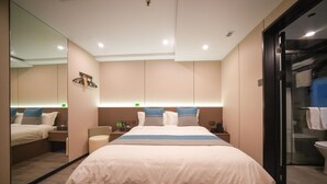 Una habitación de hotel moderna con una cama grande, una mesita de noche, un espejo y una cabina de ducha de vidrio.