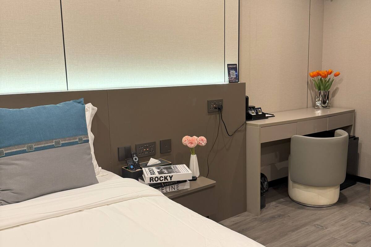 A hotel room with a bed, a desk, and an air conditioning unit.