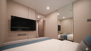 A modern hotel room with a large bed, a flat-screen TV mounted on the wall, and a large mirror reflecting the room. - Ha Fa Villa  (Hong Kong Island)