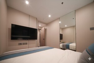 Habitación de hotel moderna con una cama grande, un televisor de pantalla plana en la pared y un espejo grande que refleja el cuarto.
