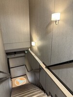 Una escalera moderna en un hotel con pared texturizada, barandilla y lámpara.
