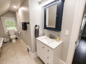 A bathroom with a toilet, sink, and mirror. - Charming Historic 5BR Home • Close to Universities, Hospital & Downtown (Flint)