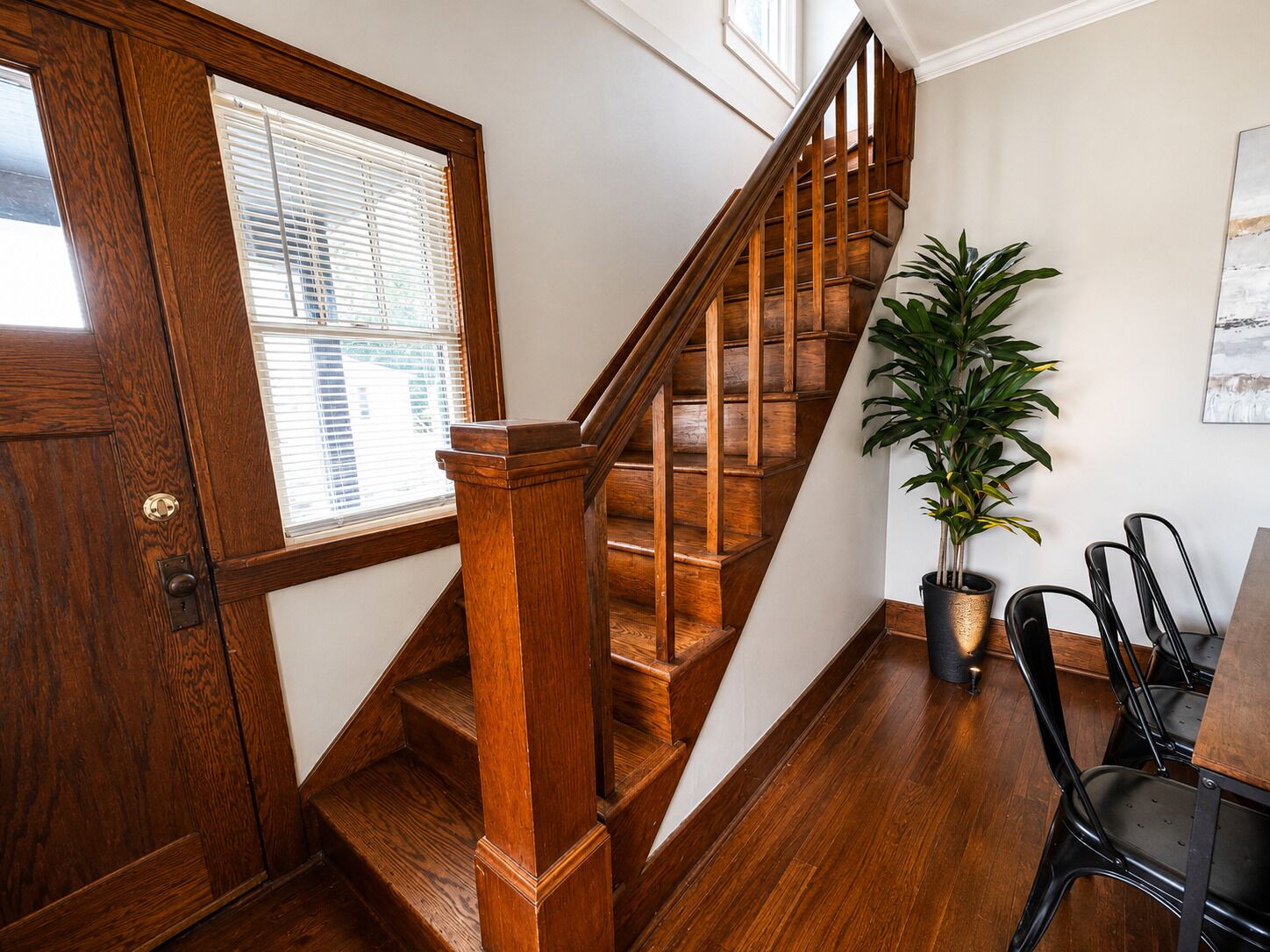 A wooden staircase with a handrail, a potted plant, and a dining area with chairs.