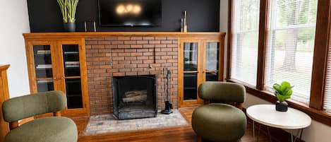 Una sala de estar con chimenea de ladrillo, un televisor de pantalla plana y dos sillones verdes.