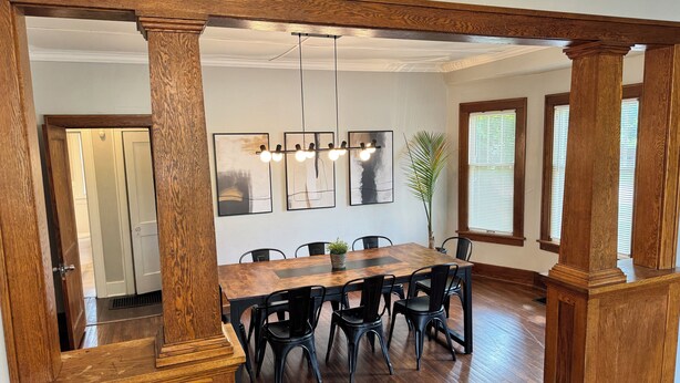 A dining area with a wooden table and chairs, a chandelier, and artwork on the wall. - Charming Historic 5BR Home • Close to Universities, Hospital & Downtown (Flint)