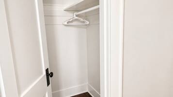 A small, white-walled closet with a hanging rod and a laundry basket.