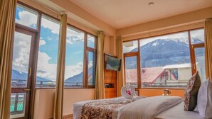 Une chambre d’hôtel équipée d’un lit, d’une télévision et de grandes fenêtres donnant sur les montagnes.
