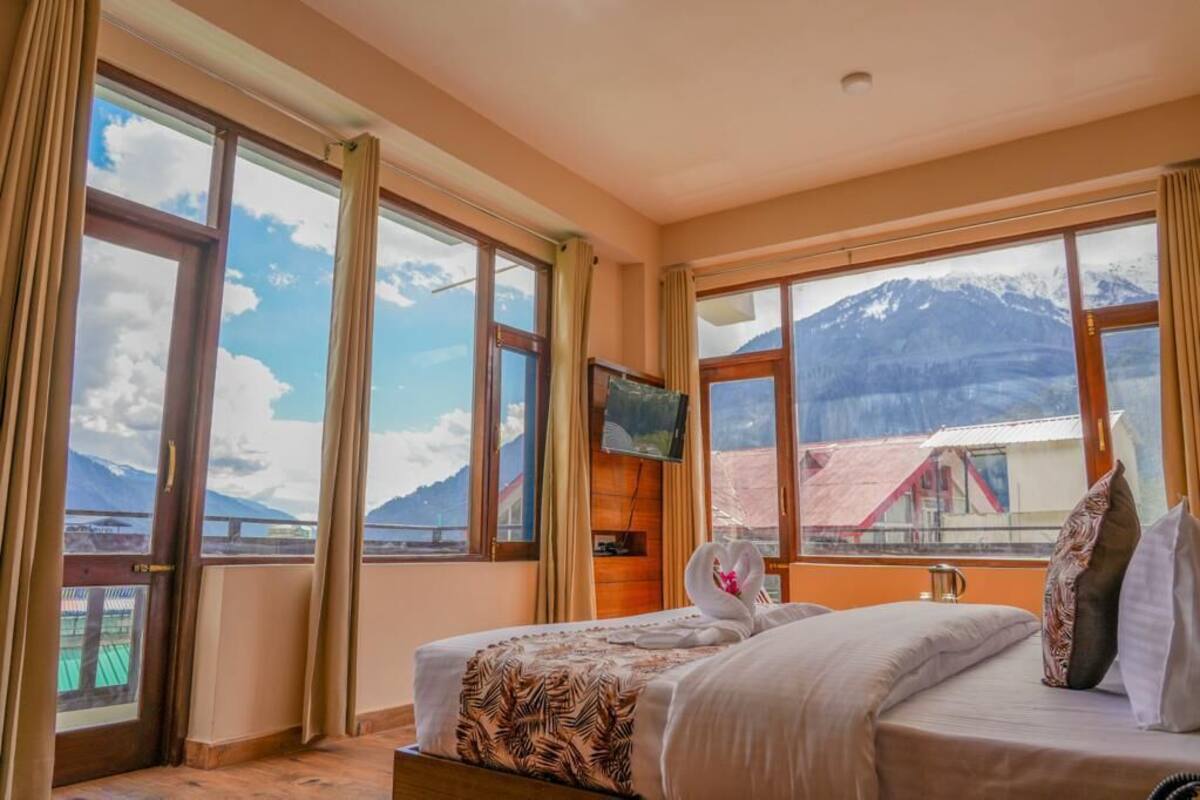 Ein Hotelzimmer mit einem Bett, einem Fernseher und großen Fenstern mit Blick auf die Berge.