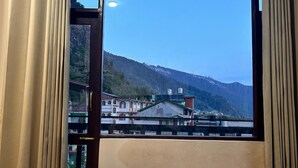 Une chambre d’hôtel dotée d’une grande fenêtre donnant sur un paysage montagneux et un pont.