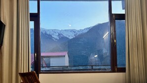 Une chambre d’hôtel dotée d’une grande fenêtre donnant sur les montagnes, d’un lit recouvert d’une couvre-lit à motifs et d’une chaise.
