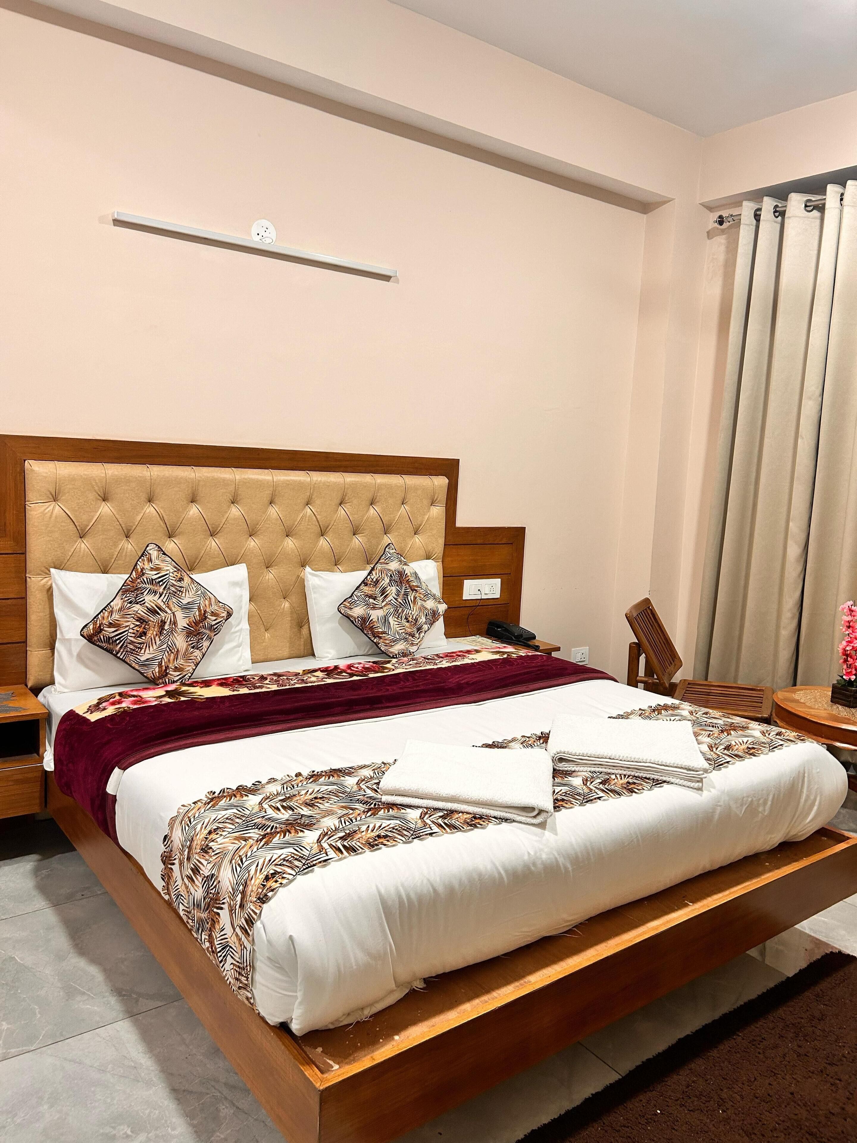 A neatly made bed with a tufted headboard, white and patterned pillows, a red throw blanket, and a floral bedspread.