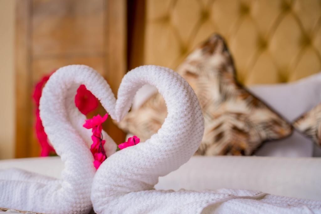 A bed with a white towel shaped like a heart and a pink flower.