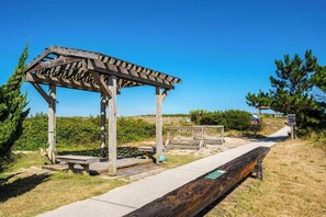 A wooden gazebo with benches, a pathway, and a bench with a blue cushion. - Dog Friendly, Hot Tub, & Walk to Beach! (Southern Shores)