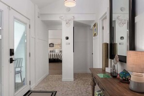 A hallway with a bed in the background, a wooden bench, a mirror, and a lamp. - Dog Friendly, Hot Tub, & Walk to Beach! (Southern Shores)