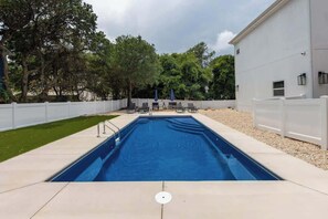 Ein rechteckiger Pool mit weißem Zaun, Liegestühlen und Sonnenschirmen.