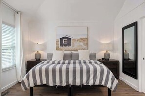 Ein Schlafzimmer mit einem Bett, zwei Nachttischen, einer Wandleuchte, einem gerahmten Bild und einem großen Spiegel.