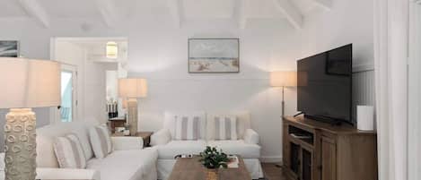 A modern living room with a white sofa, a wooden coffee table, a flat-screen TV, and a framed picture on the wall.