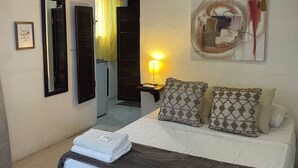 A hotel room with a bed, a bedside table with a lamp, a mirror, a framed picture, and a door leading to a bathroom. - Downtown Studio for 3 w Kitchen (Isla Mujeres)
