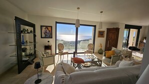 A spacious living room with a large window offering a view of the sea, furnished with a sofa, chairs, and a coffee table. - Master villa for 14 people with air conditioning (LES ISSAMBRES)